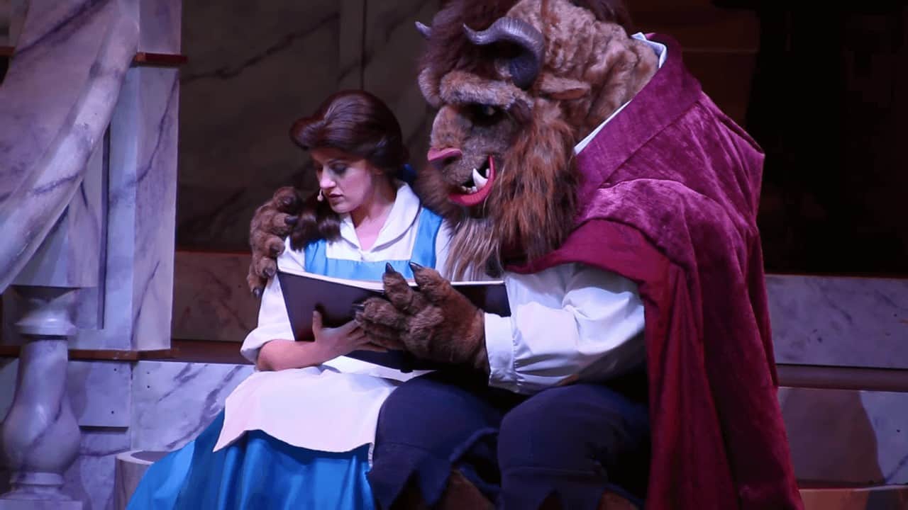 Belle reading a book to the Beast in the live stage show